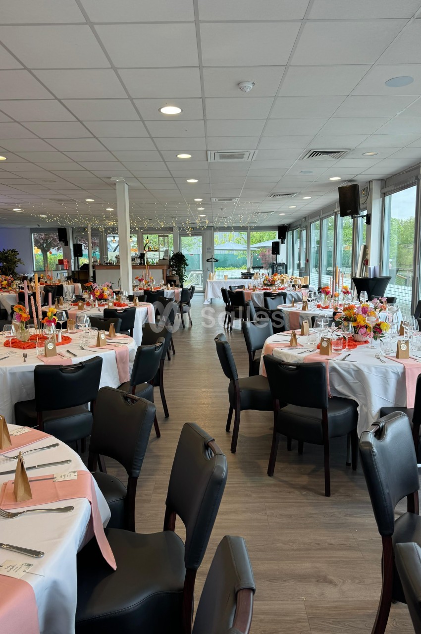 Salle de réception élégamment décorée avec des tables rondes, nappes blanches et accents roses, prête pour un événement.