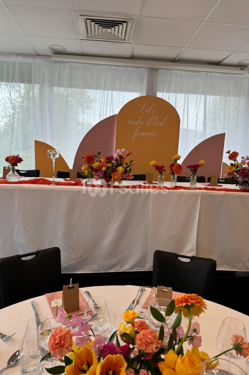Table décorée avec des fleurs colorées et arrière-plan avec un panneau pastel portant un message en anglais.