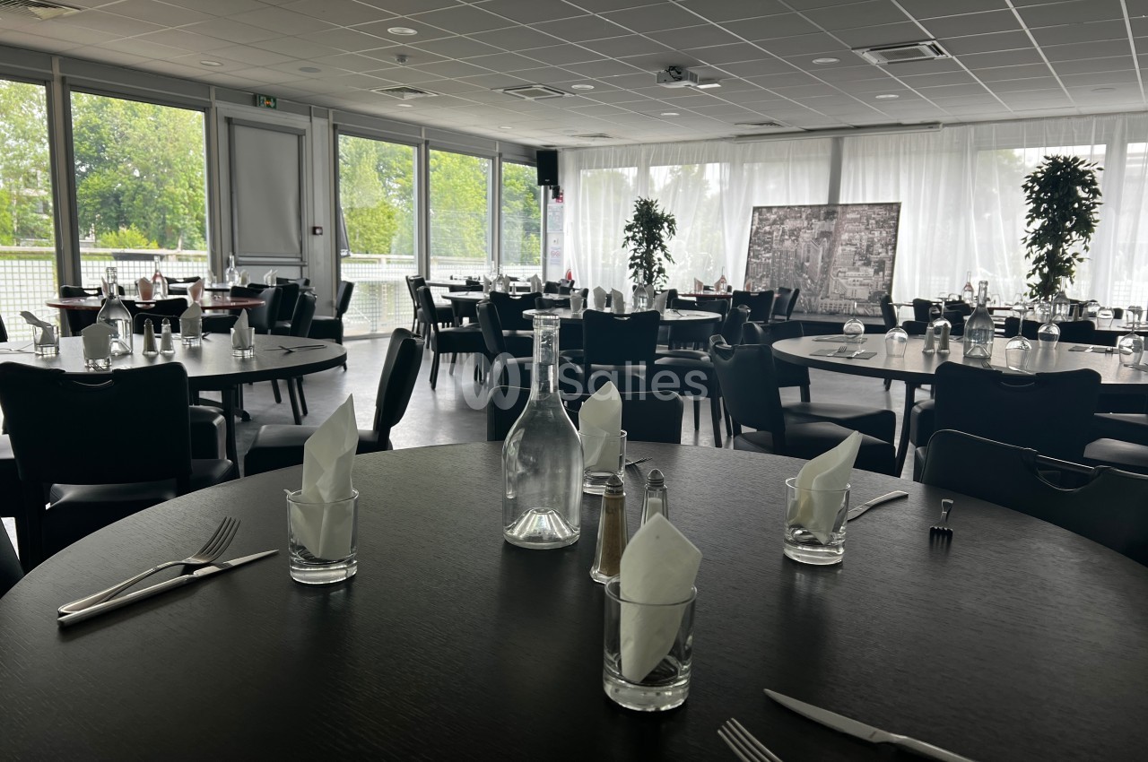 Salle de restaurant lumineuse avec tables dressées, grandes baies vitrées donnant sur un espace extérieur verdoyant.