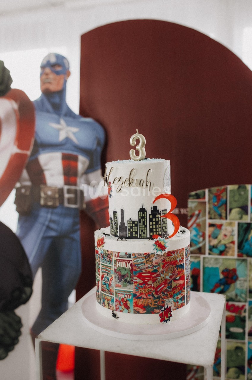 Gâteau d'anniversaire à trois étages décoré sur le thème des super-héros, avec un chiffre 3 au sommet.