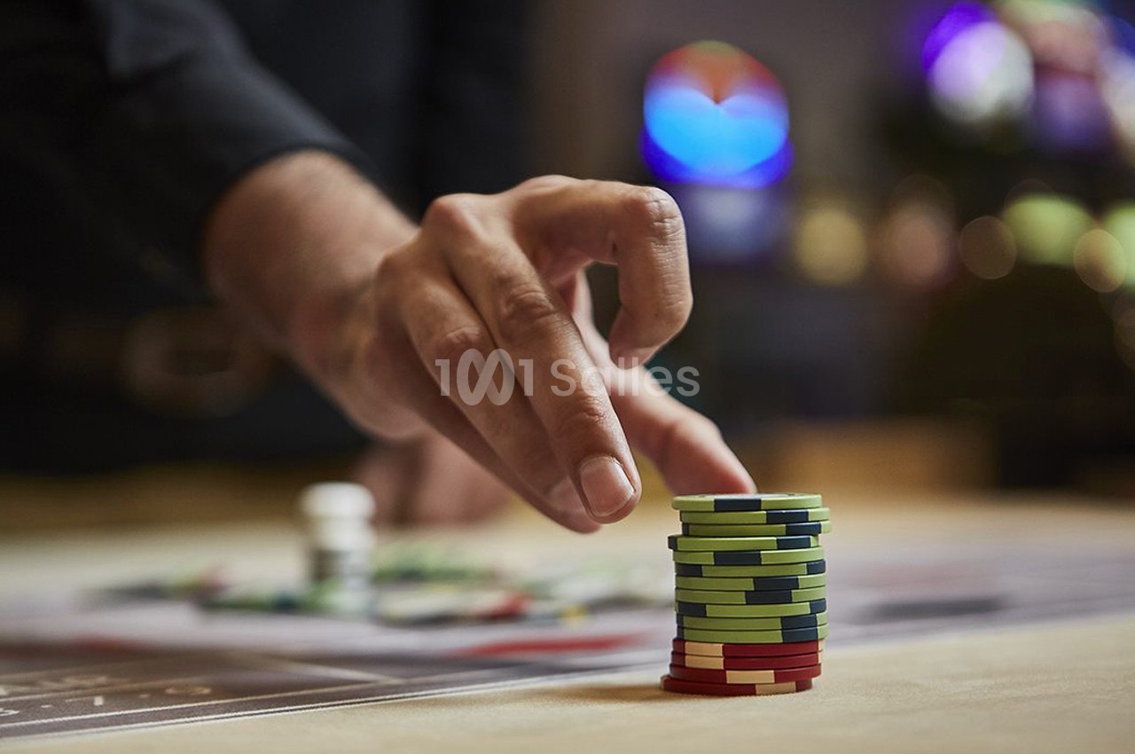 Main empilant des jetons de casino colorés sur une table, avec un arrière-plan flou de lumières et de jeux.