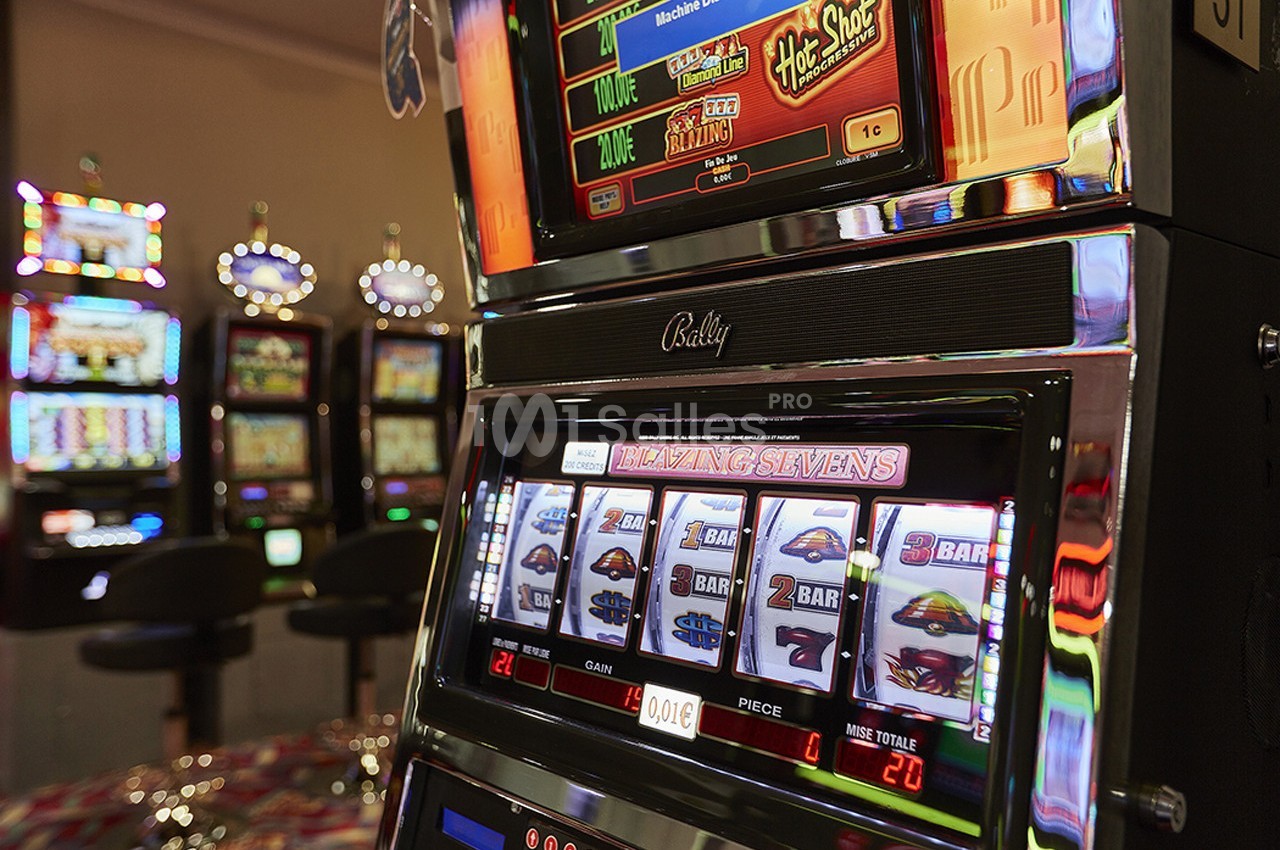 Machine à sous allumée dans un casino, avec des rouleaux affichant des symboles et d'autres machines en arrière-plan.