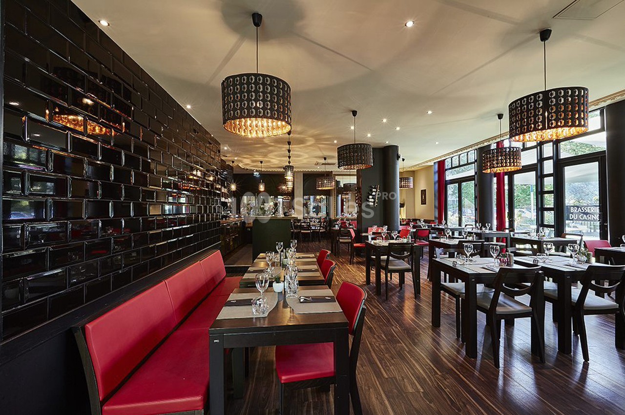 Salle de restaurant moderne avec tables dressées, banquettes rouges, murs noirs brillants et grandes fenêtres.