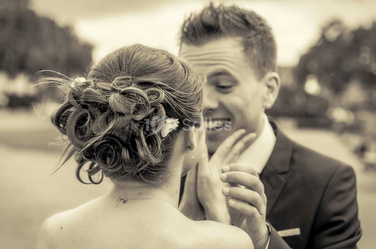 Un couple en tenue de mariage échange un moment complice dans un parc, vu de dos pour la mariée.