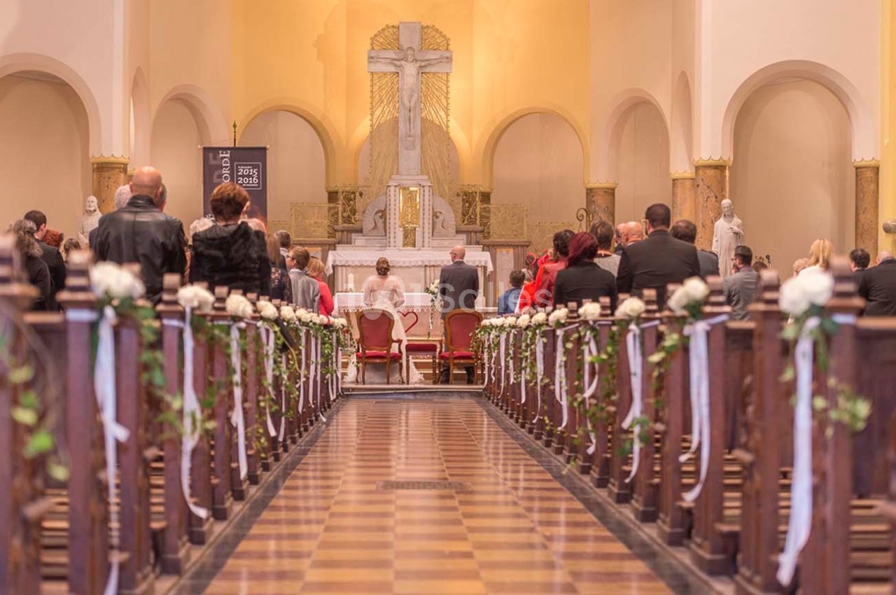 Des personnes assistent à une cérémonie religieuse dans une église décorée de fleurs blanches.