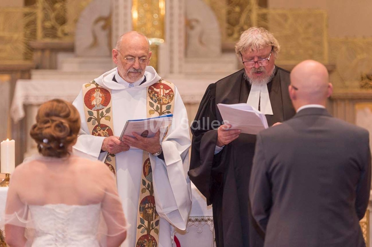 Deux officiants religieux dirigent une cérémonie de mariage devant un couple dans une église.