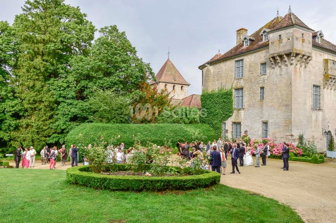 Groupe de personnes rassemblées dans un jardin devant un château entouré de verdure et de rosiers.