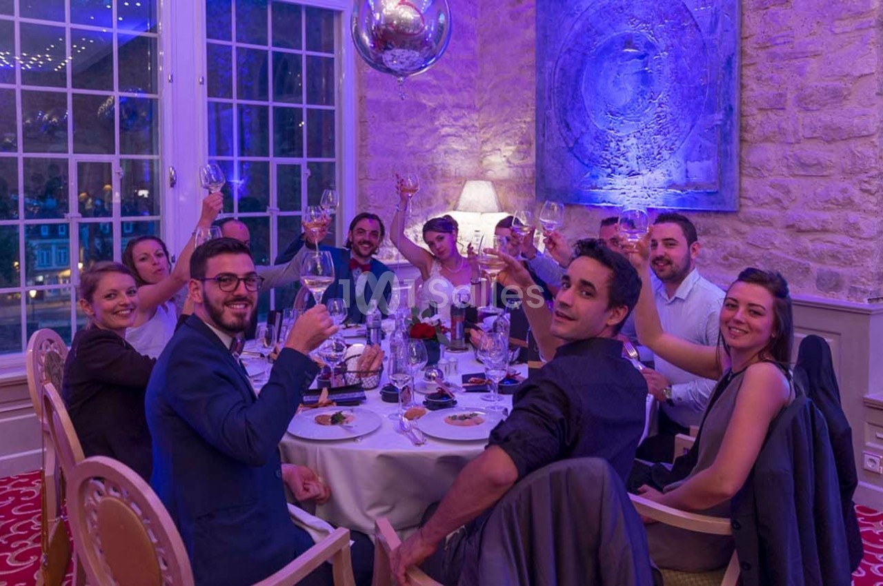 Un groupe de personnes souriantes trinque autour d'une table dressée dans une salle élégante avec un mur en pierre.