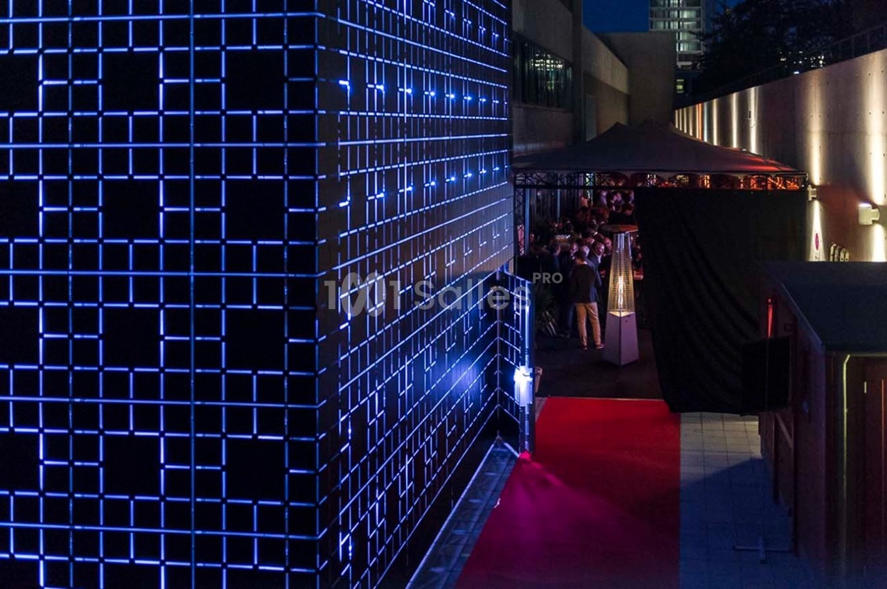 Façade illuminée par des motifs géométriques bleus, avec un tapis rouge menant à une entrée sous un auvent.