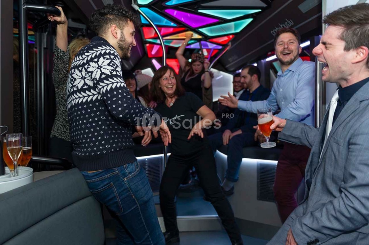 Des personnes rient et dansent dans un bus aménagé avec des lumières colorées, ambiance festive.