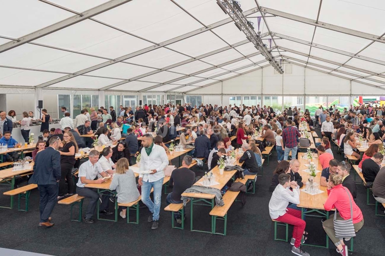 Des personnes assises et debout dans une grande tente, partageant un repas ou discutant lors d'un événement collectif.