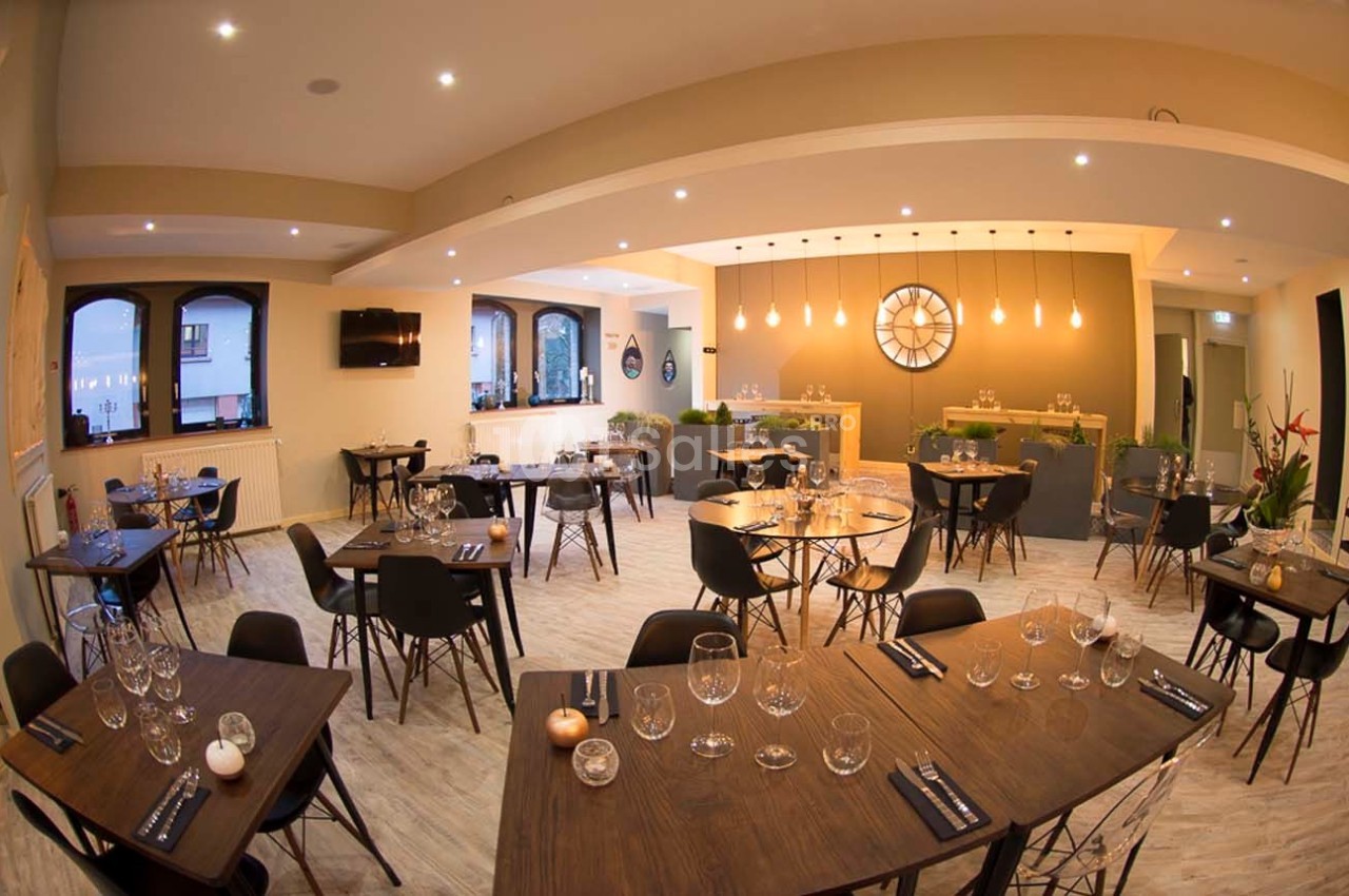 Salle de restaurant moderne avec tables en bois, chaises noires, éclairage chaleureux et grande horloge murale.