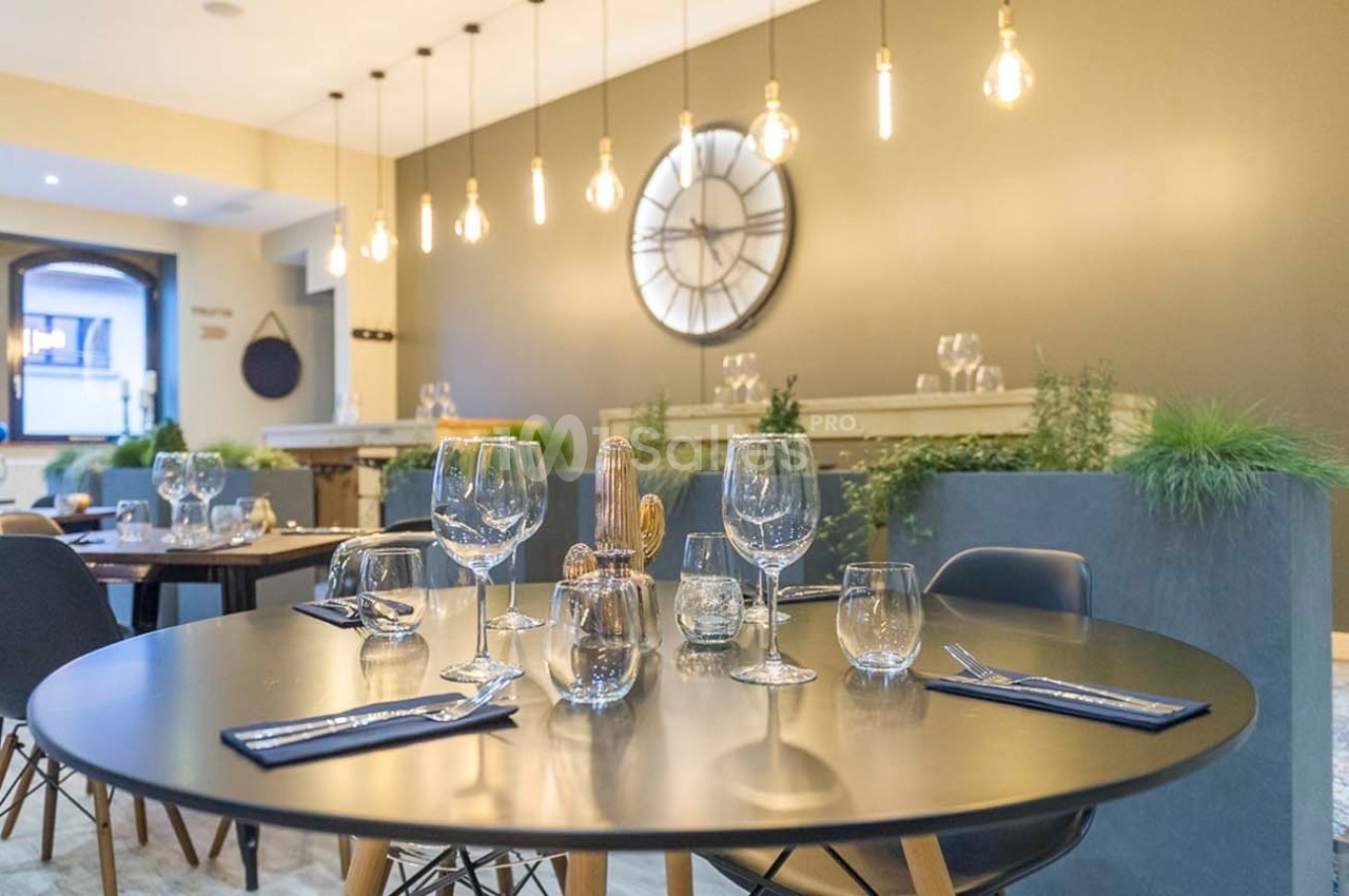 Salle de restaurant moderne avec table dressée, décorée de plantes et éclairée par des suspensions lumineuses.