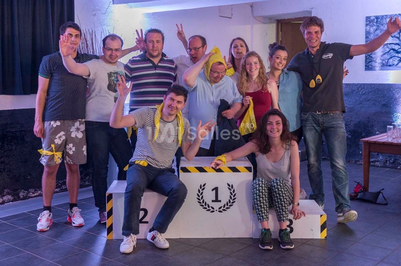 Un groupe de personnes souriantes posant autour d'un podium numéroté dans une ambiance festive en intérieur.
