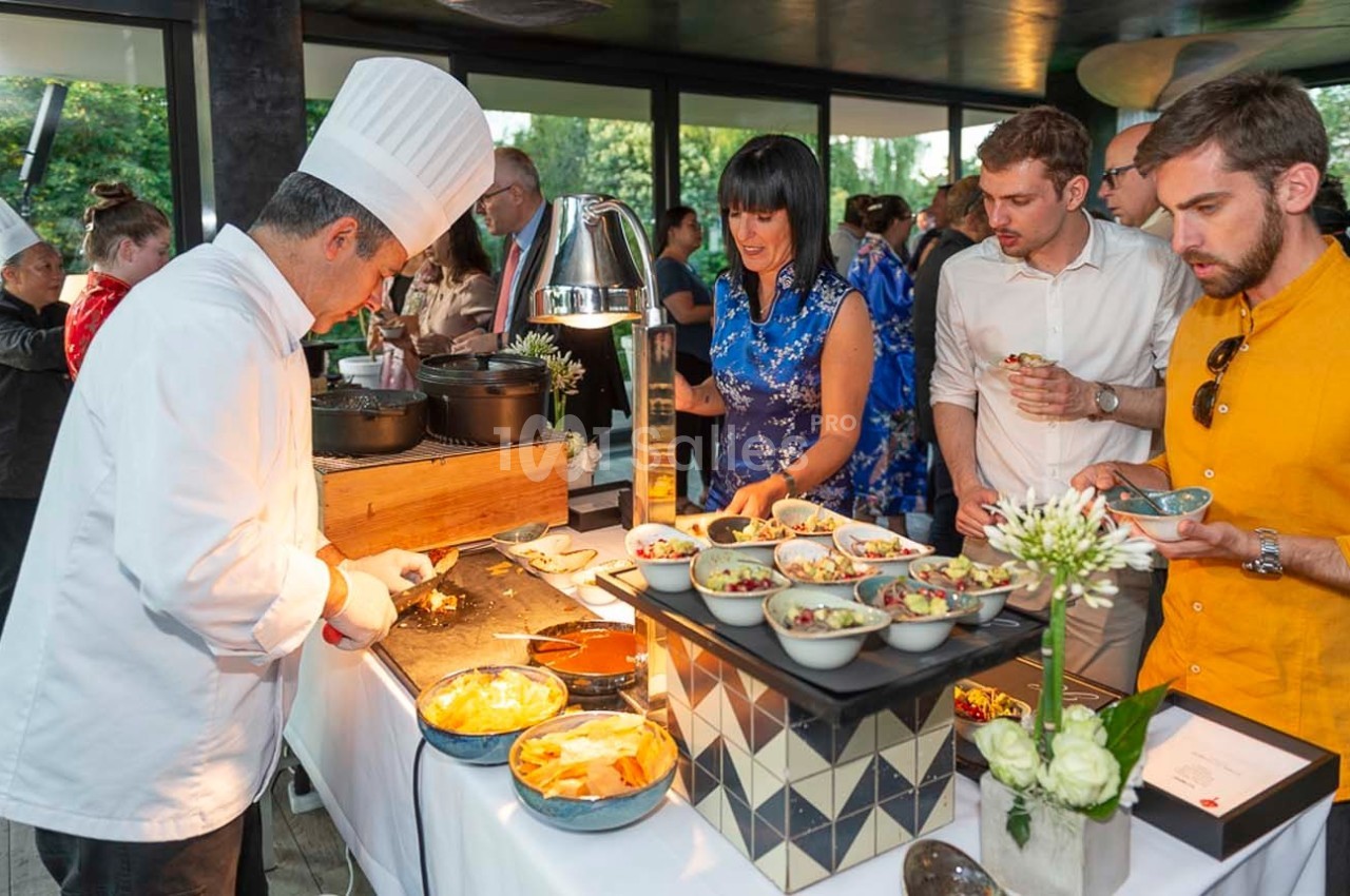 Un chef prépare des plats devant des convives lors d'un buffet dans un cadre lumineux et moderne.