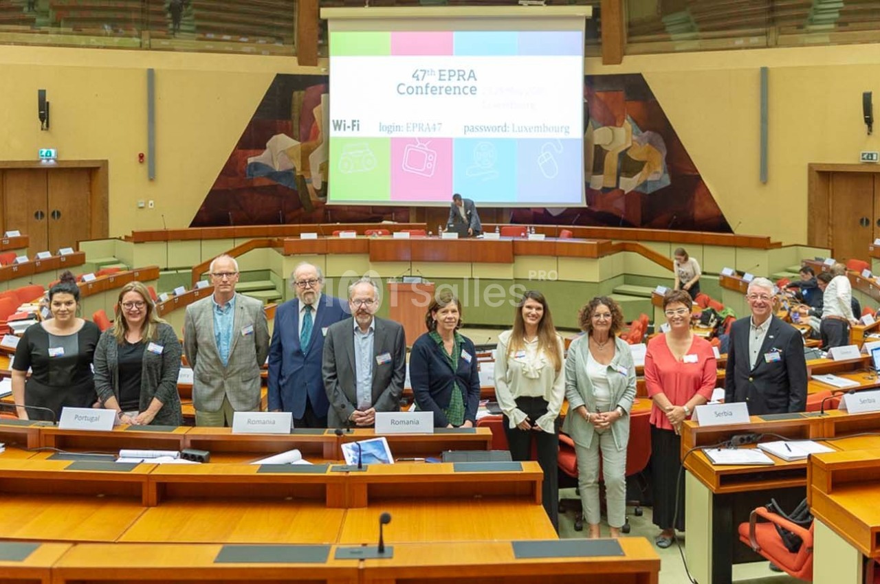 Un groupe de personnes posant devant des tables dans une salle de conférence avec un écran affichant des informations.