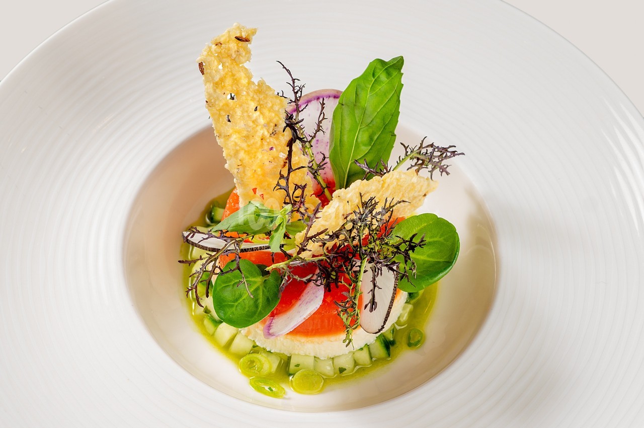 Assiette gastronomique avec légumes frais, herbes, radis, saumon et tuiles croustillantes, présentée de manière artistique.