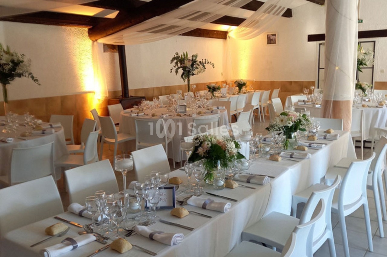 Salle de réception décorée avec des tables dressées, nappes blanches, compositions florales et éclairage chaleureux.