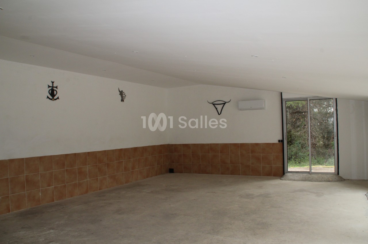 Salle vide avec sol en béton, murs partiellement carrelés, décorations murales et porte vitrée donnant sur l'extérieur.