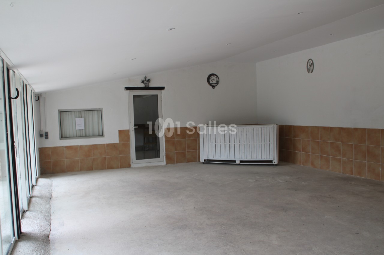 Salle vide avec sol en béton, murs blancs partiellement carrelés, une porte, une fenêtre et un radiateur blanc.