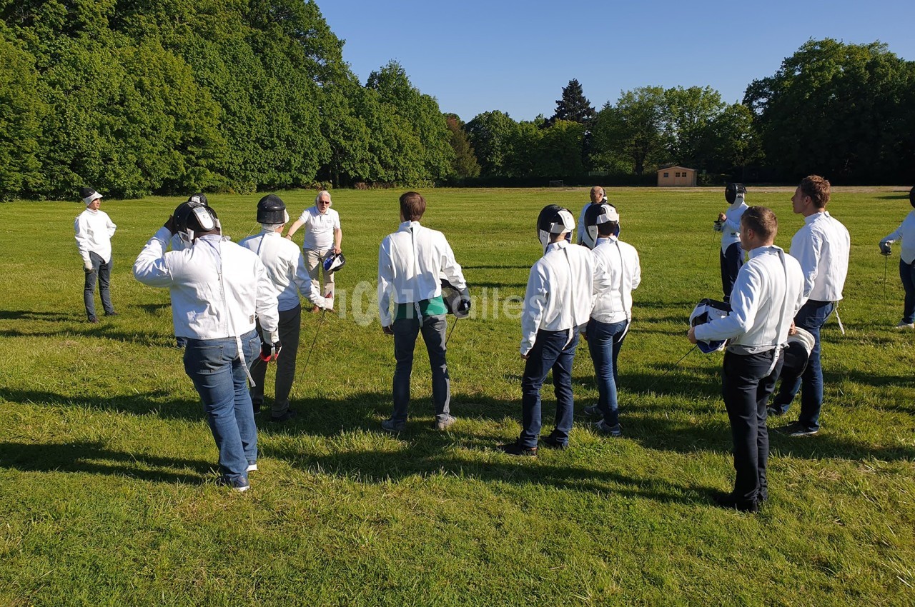 Un groupe de personnes en tenue de protection écoute un instructeur dans un champ verdoyant.