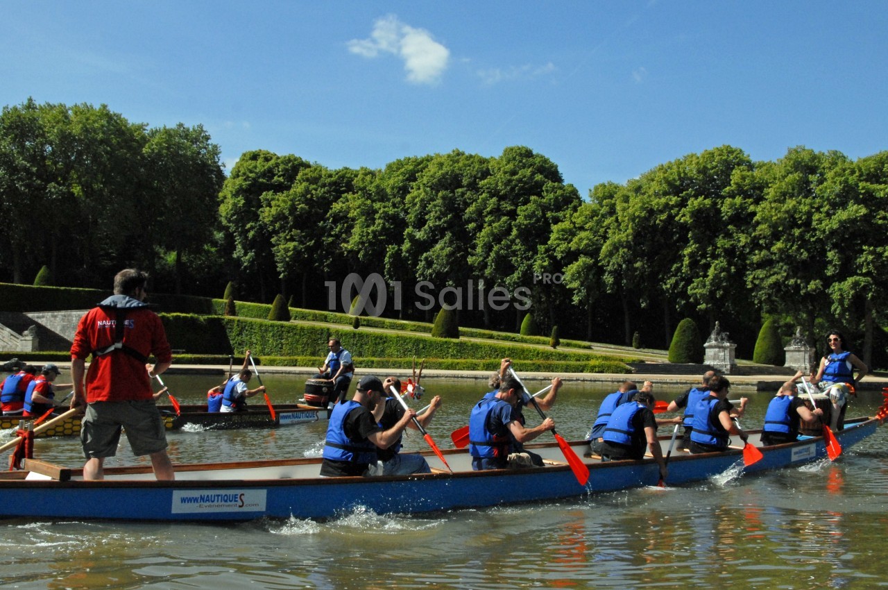 Des personnes pagayant en équipe sur des barques dans un plan d'eau entouré d'arbres et de verdure.