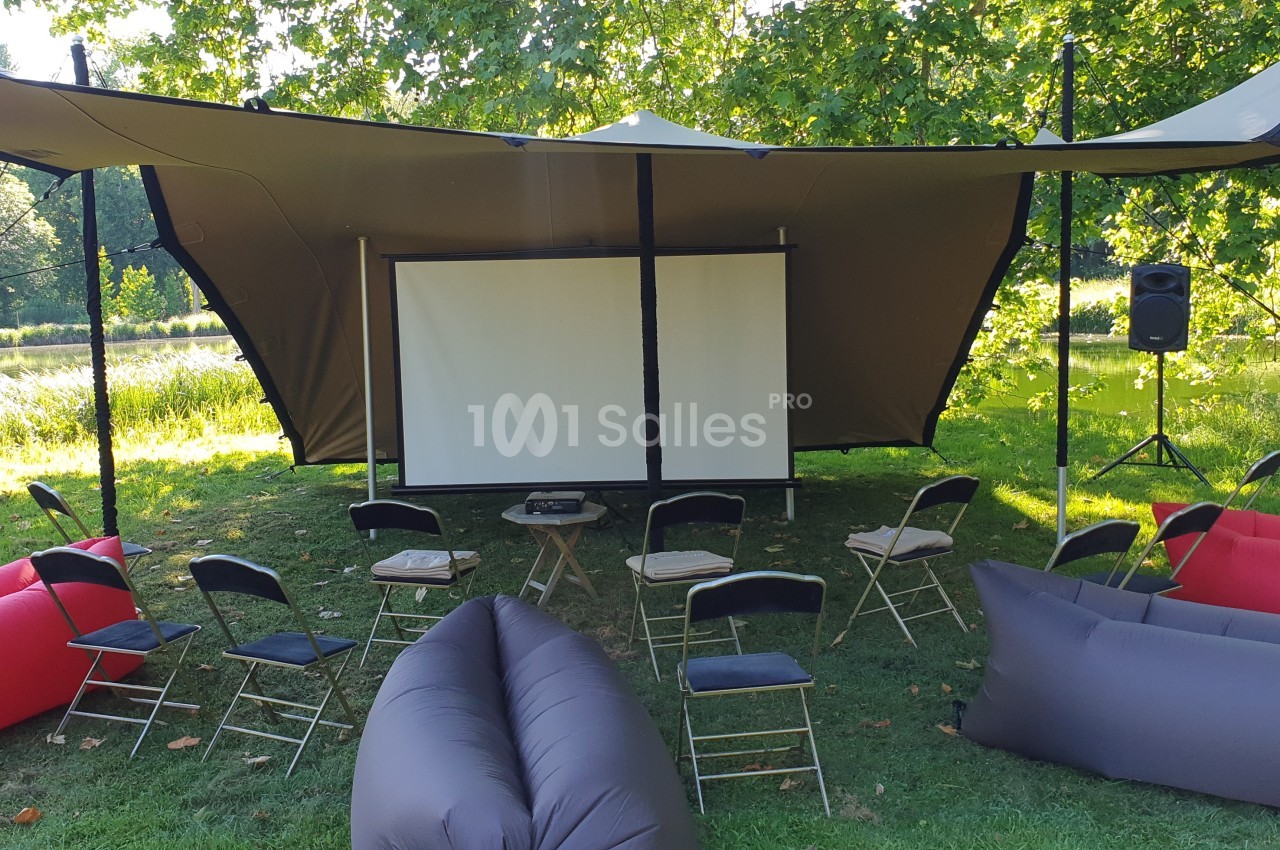 Écran de projection installé en extérieur sous une toile tendue, entouré de chaises et de poufs gonflables.