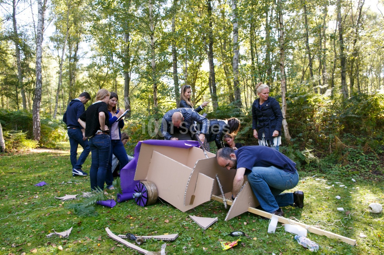 Des personnes assemblent une structure en carton dans une clairière boisée lors d'une activité de groupe.