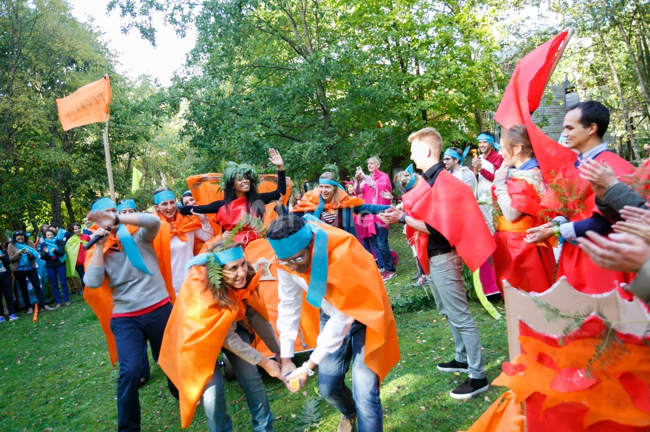 Des personnes participent à une activité en plein air, vêtues de costumes colorés, entourées d'arbres et d'observateurs.