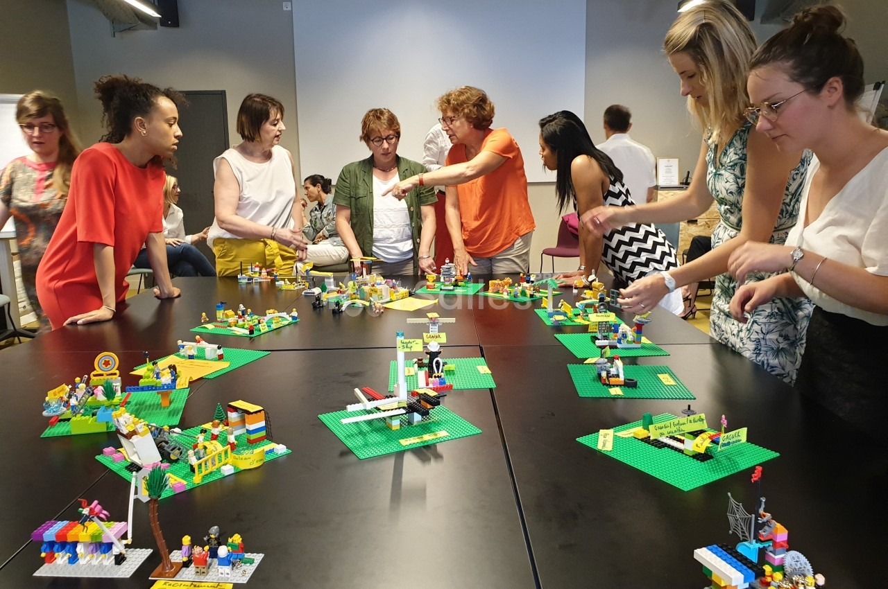 Des personnes collaborent autour de tables noires avec des constructions en Lego dans une salle de réunion.