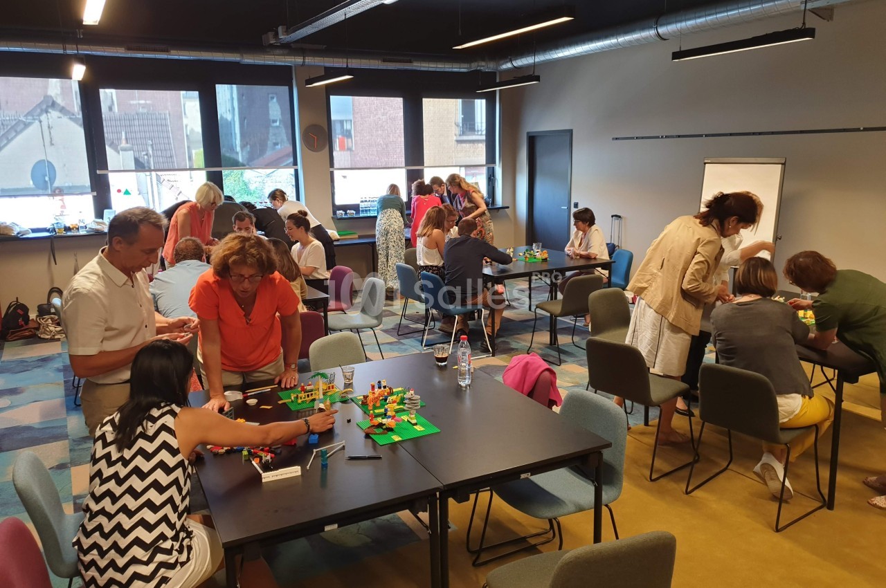Des personnes participent à un atelier collaboratif autour de tables, utilisant des briques colorées dans une salle…