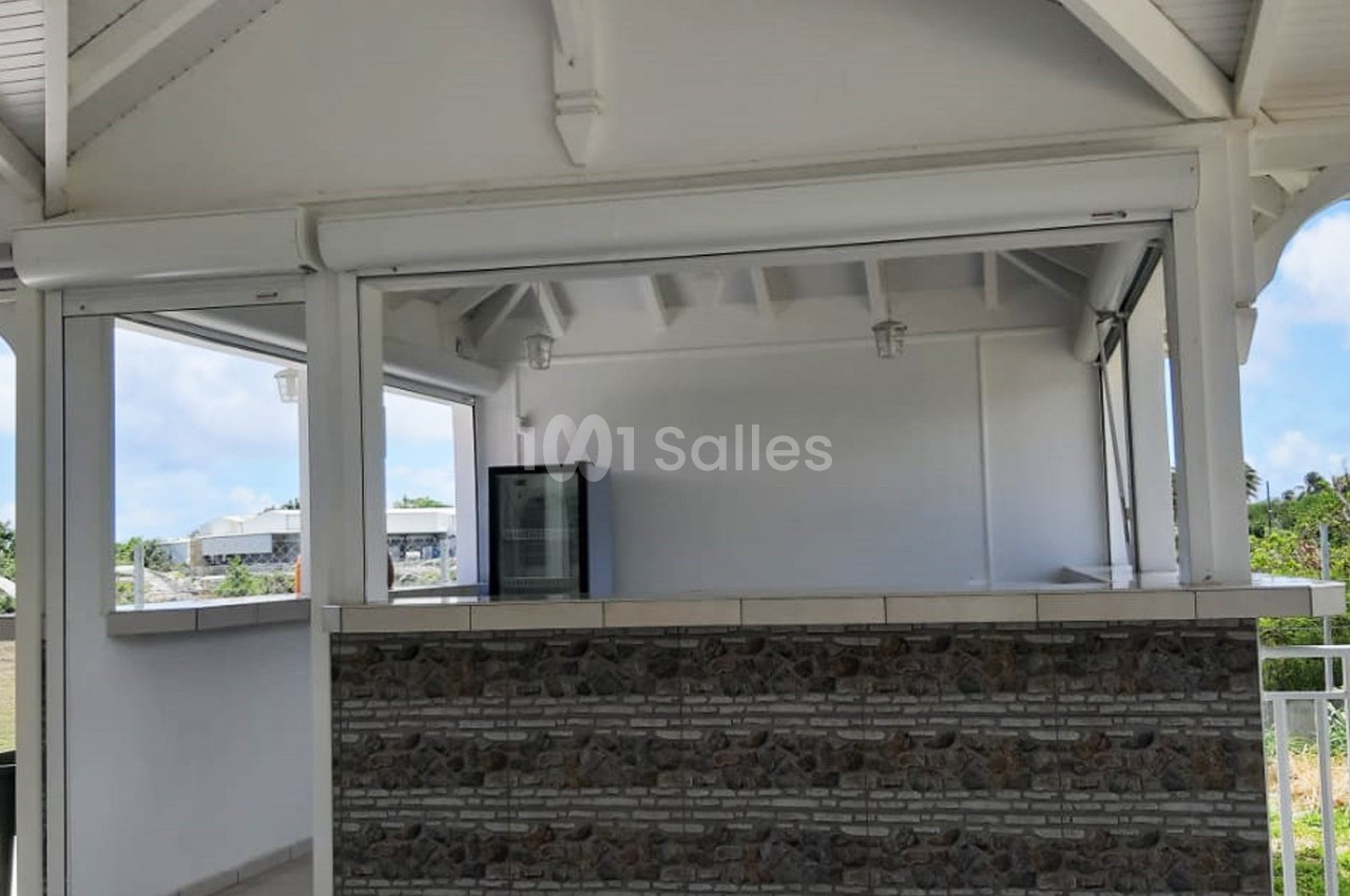 Abri extérieur avec comptoir en pierre, réfrigérateur visible à l'intérieur et structure en bois blanc.