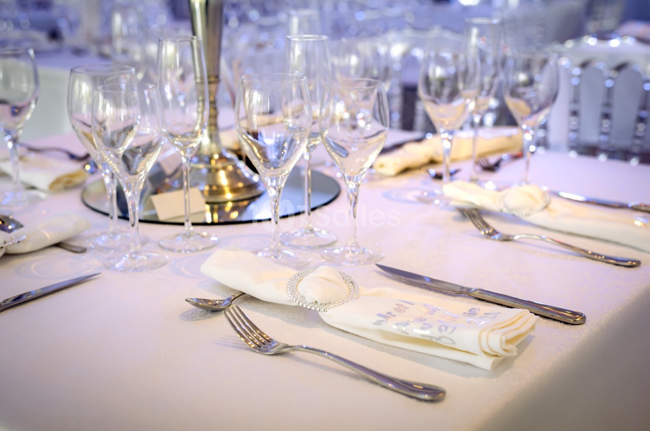 Table élégamment dressée avec nappes blanches, verres à pied, couverts en argent et serviettes pliées.