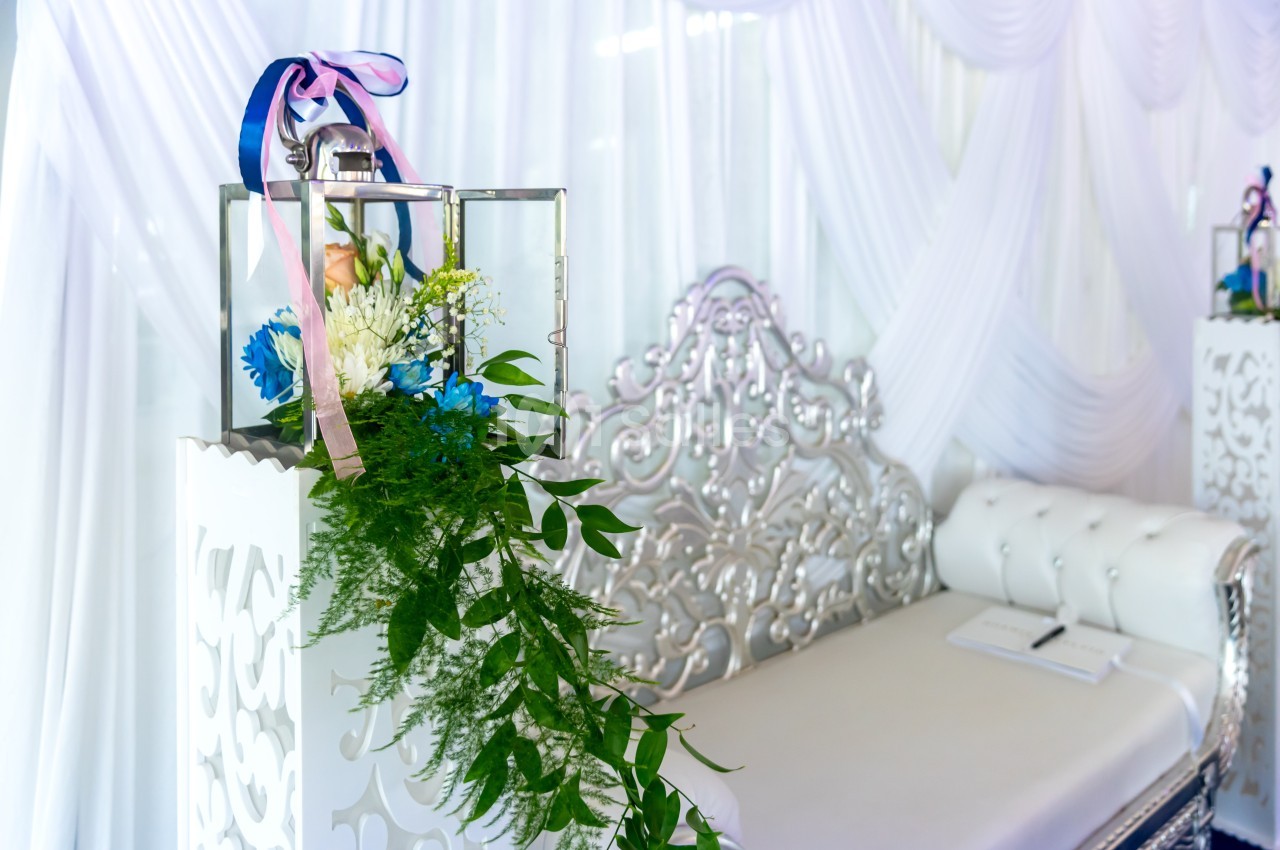 Décoration florale avec des rubans et des feuillages sur un support blanc, devant un canapé argenté capitonné.