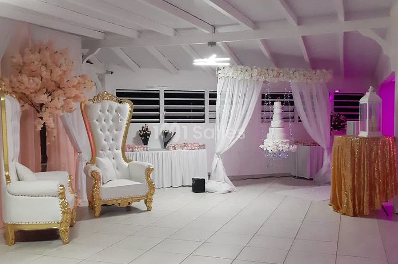 Salle décorée pour un événement avec fauteuils blancs dorés, arche fleurie, table dorée et arbre artificiel rose.