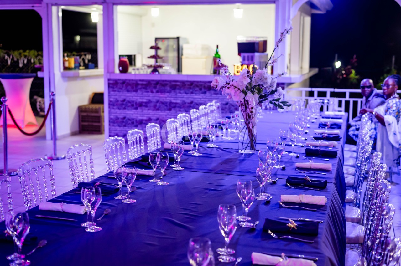 Table élégamment dressée avec nappes noires, verres et serviettes, dans un espace lumineux avec bar en arrière-plan.
