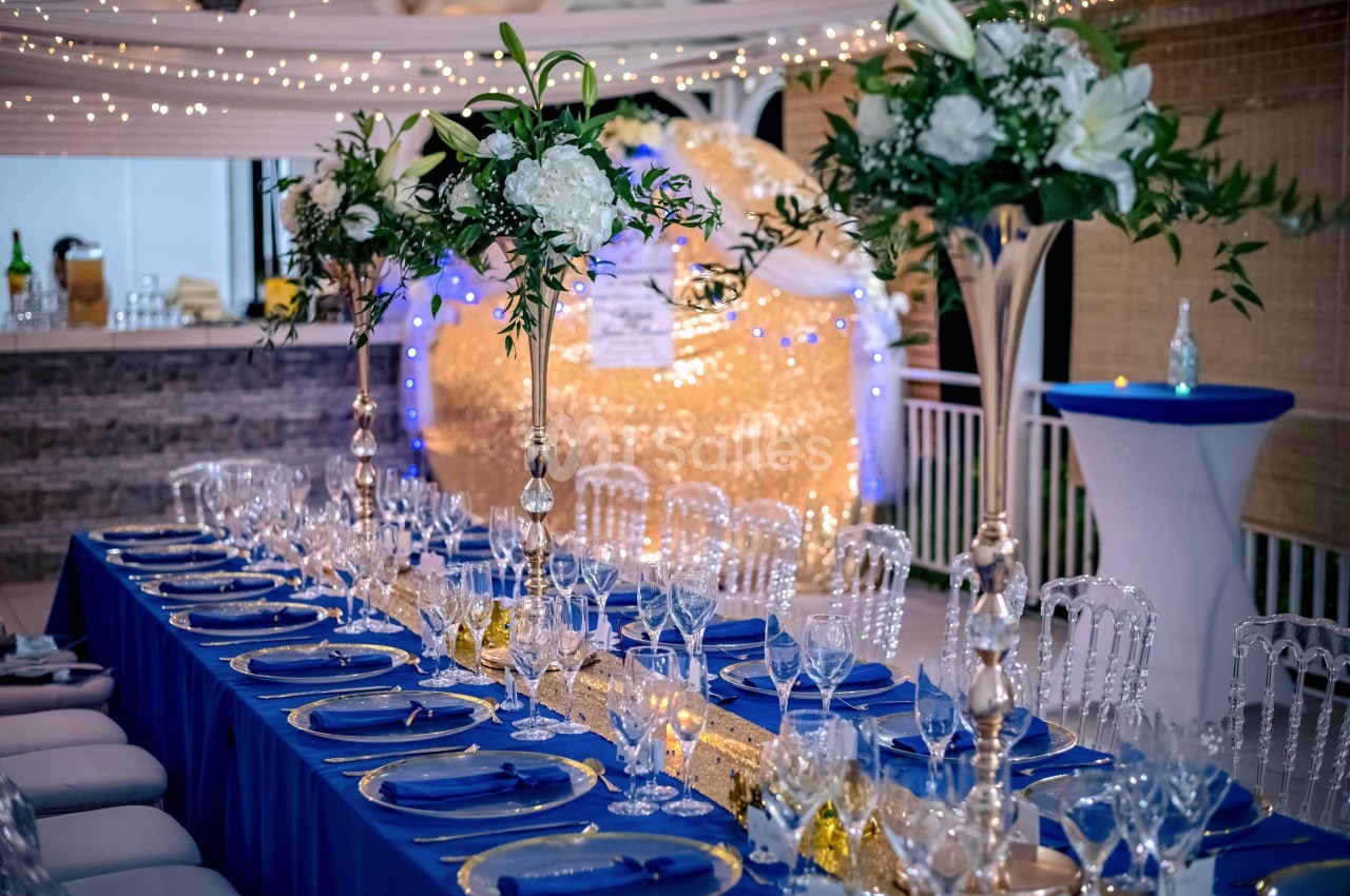 Table de réception élégamment dressée avec nappes bleues, vaisselle raffinée et décorations florales blanches et vertes.