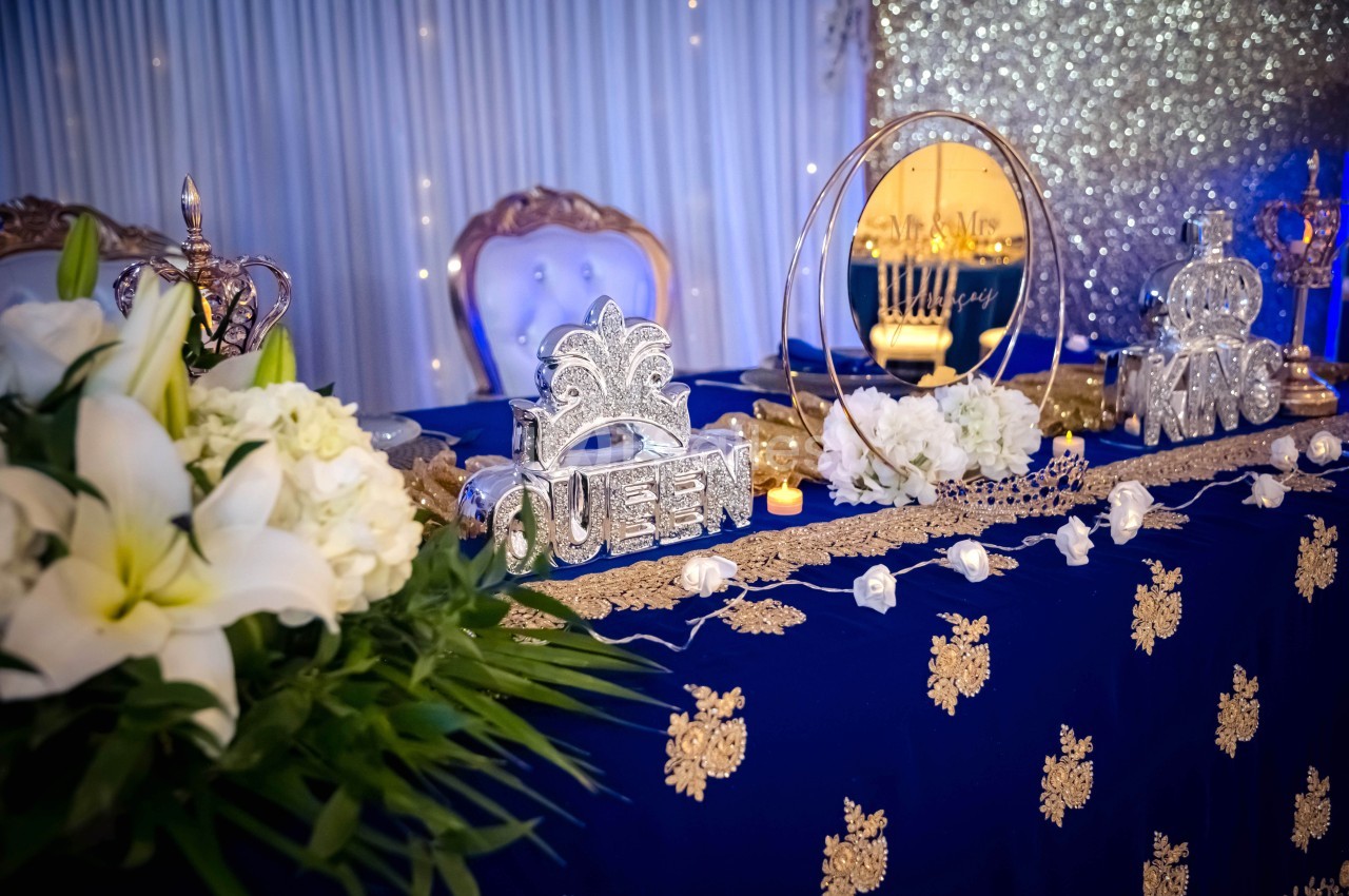 Table décorée avec des fleurs blanches, des ornements royaux ’Queen’ et ’King’, et un fond scintillant.
