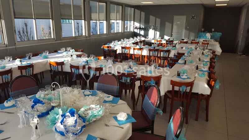 Salle de réception décorée avec des tables dressées, nappes blanches et accents bleus, prête pour un événement.