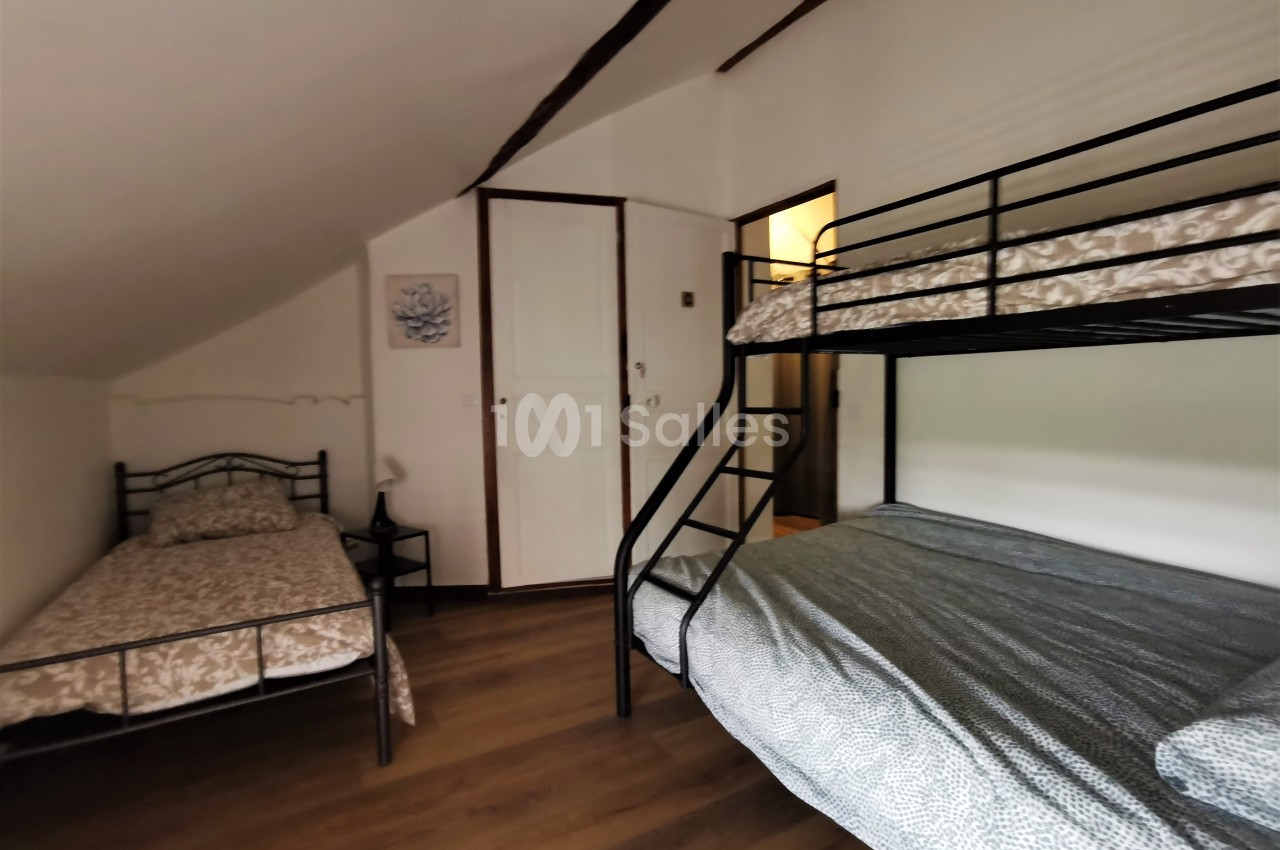 Chambre avec un lit simple et un lit superposé en métal, parquet au sol et murs blancs.