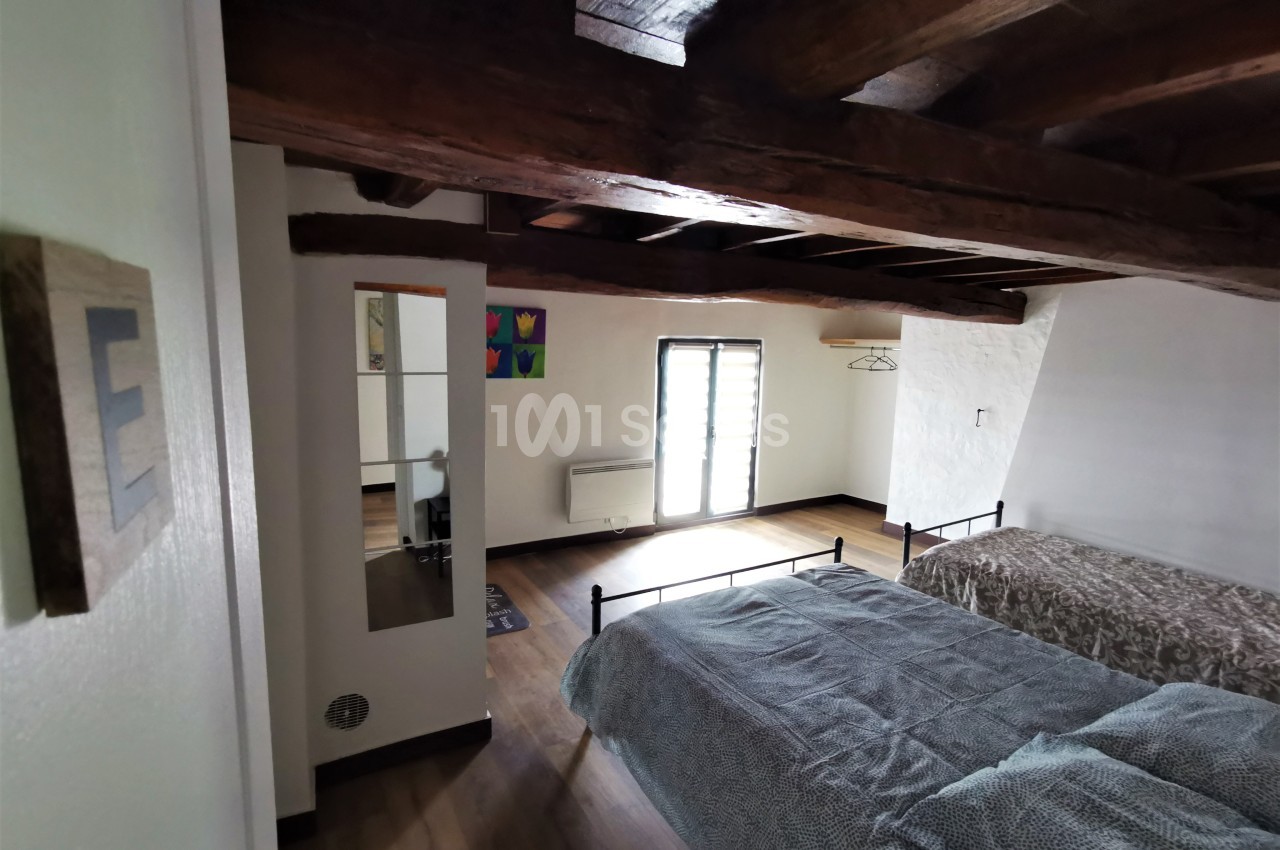 Chambre avec deux lits simples, poutres apparentes au plafond et lumière naturelle entrant par une porte-fenêtre.