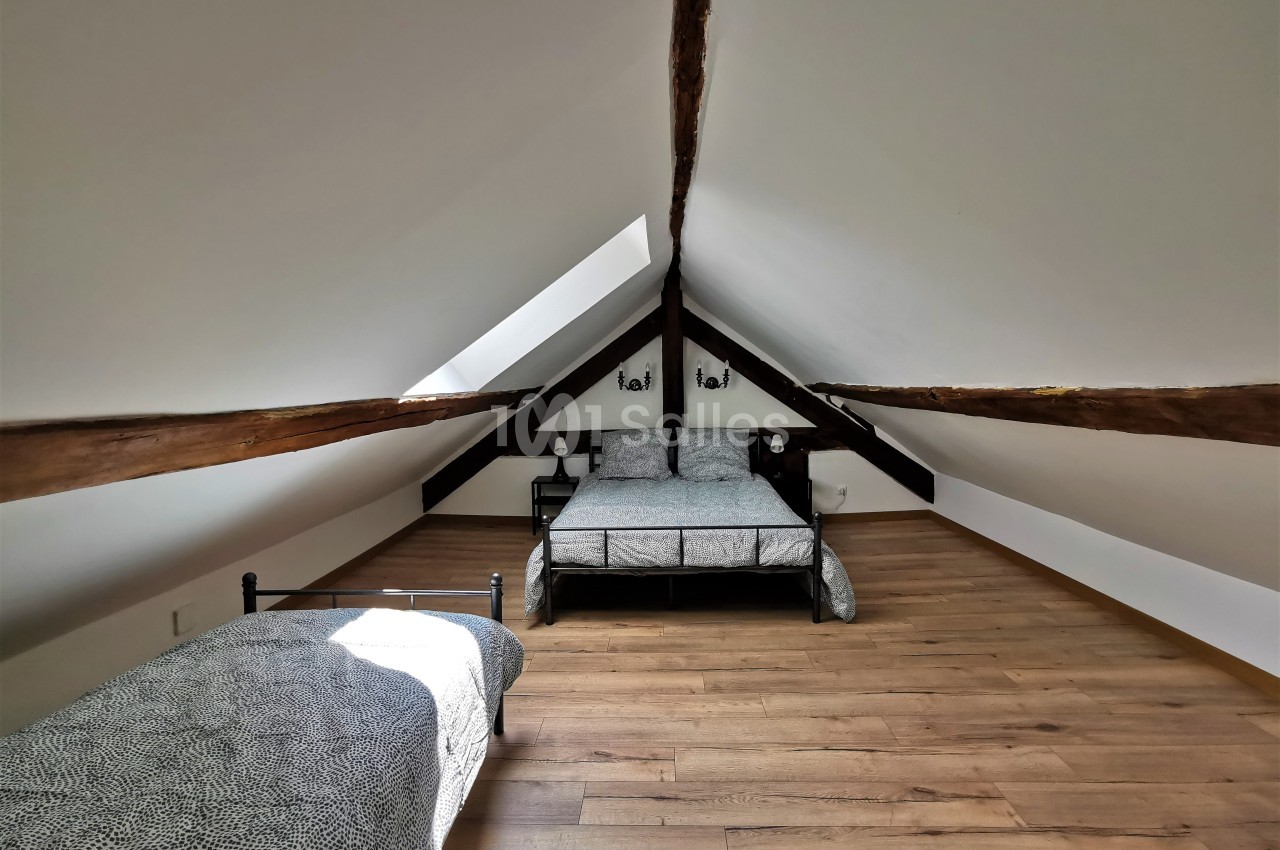Chambre mansardée avec parquet, deux lits simples, poutres apparentes et lumière naturelle provenant d'une fenêtre de toit.