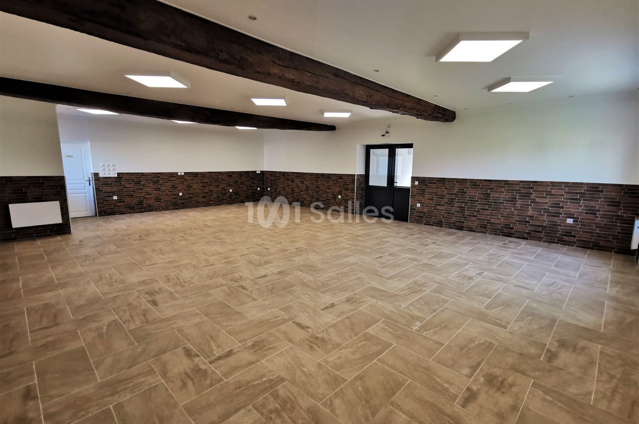 Salle vide avec sol en carrelage beige, murs mi-hauteur en briques, poutres apparentes et éclairage encastré.