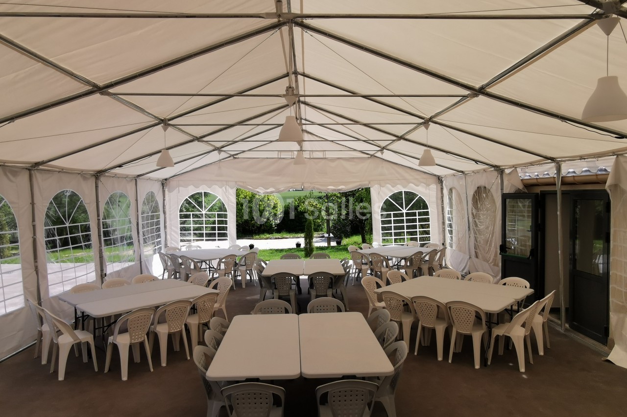 Intérieur d'une tente blanche avec des tables et des chaises en plastique disposées pour un événement.