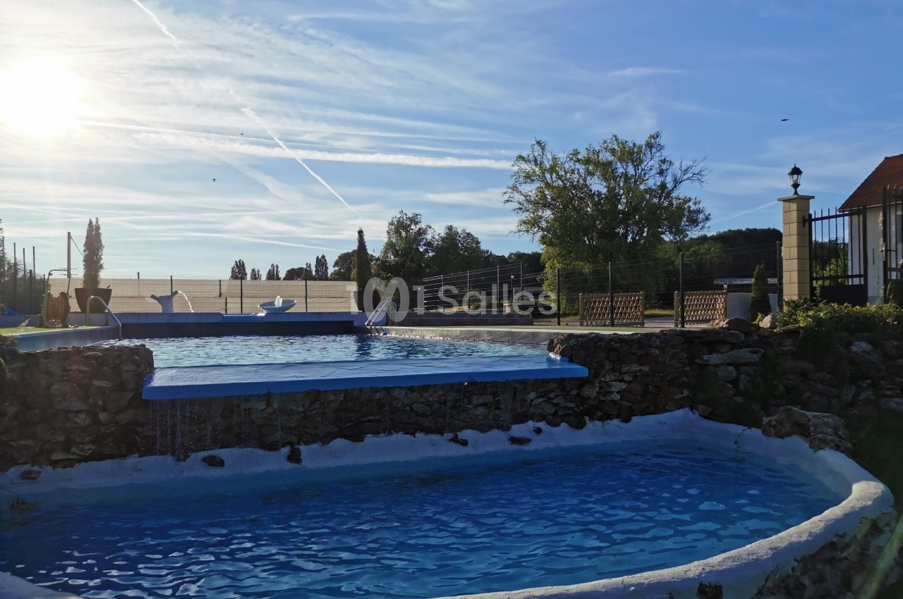 Piscine extérieure à plusieurs niveaux entourée de végétation, sous un ciel dégagé en fin de journée.