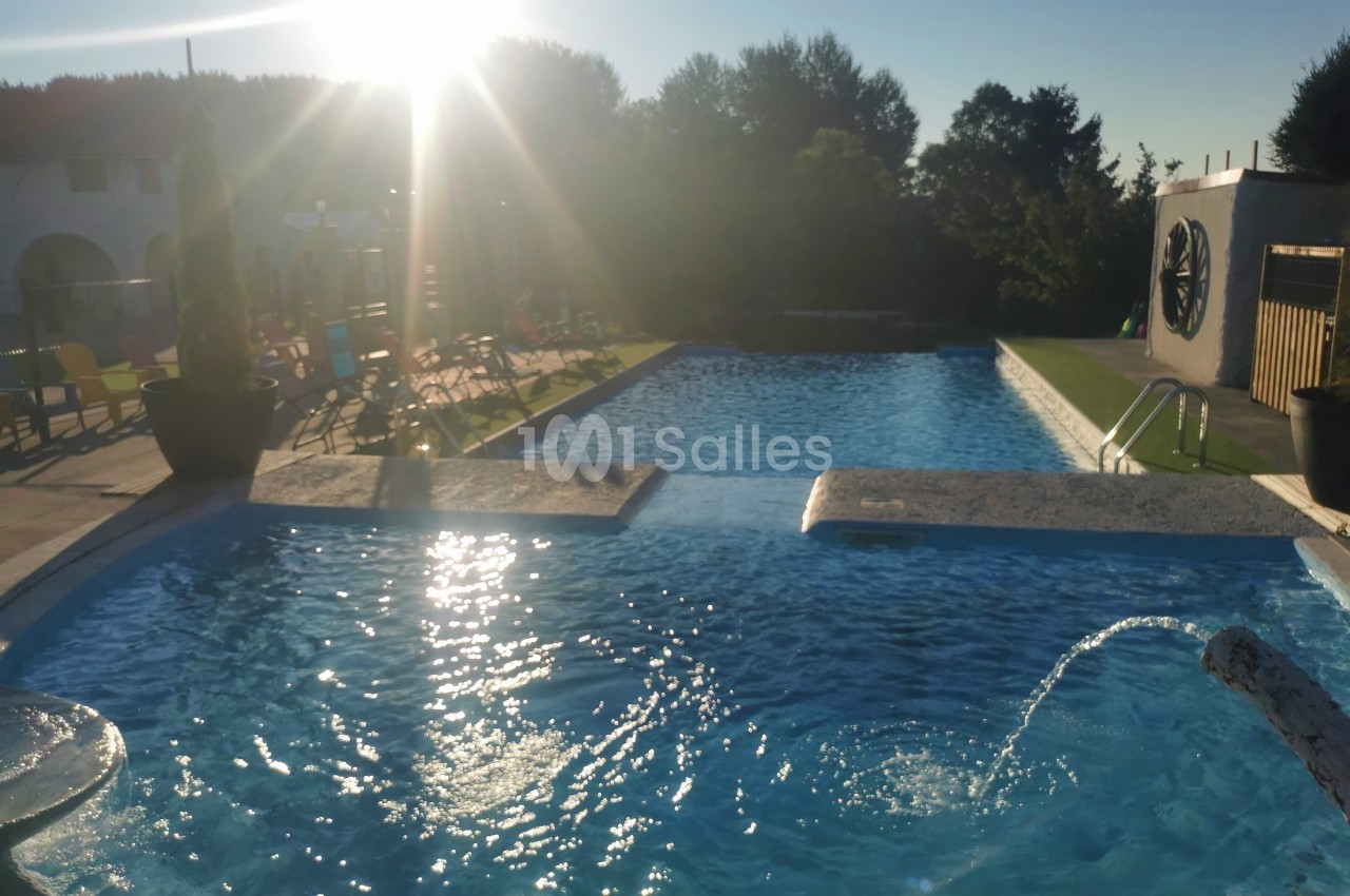 Piscine extérieure éclairée par le soleil couchant, entourée de végétation et de chaises longues.