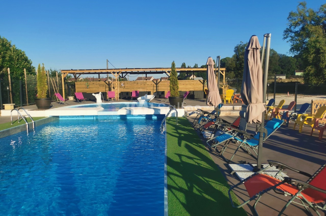 Piscine extérieure avec transats colorés, parasols et pergola en bois dans un cadre ensoleillé.