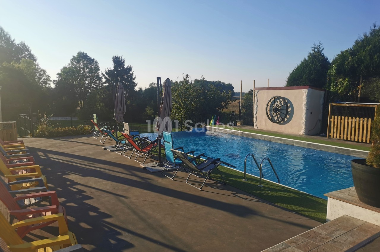 Piscine extérieure entourée de chaises longues colorées, avec parasols et vue sur un paysage arboré.