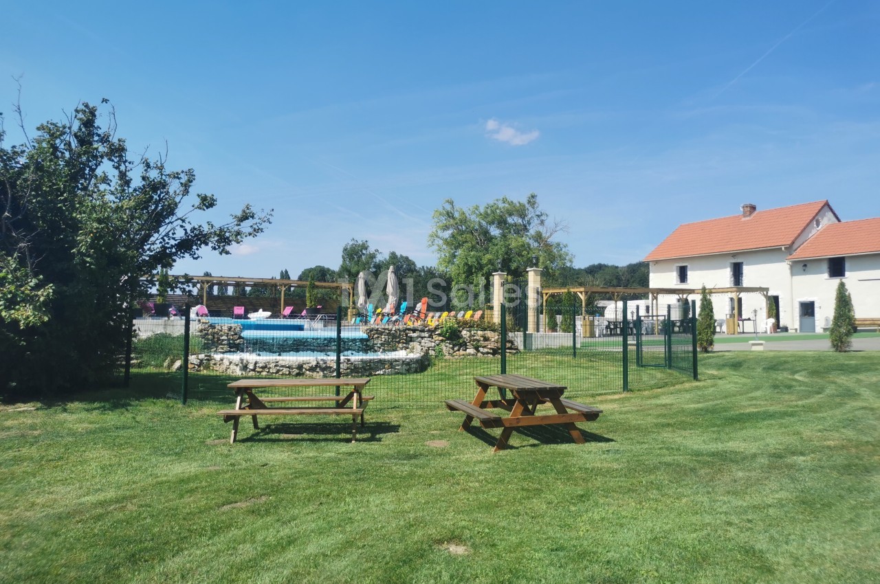 Espace extérieur avec pelouse, tables de pique-nique, piscine clôturée et bâtiments résidentiels en arrière-plan.