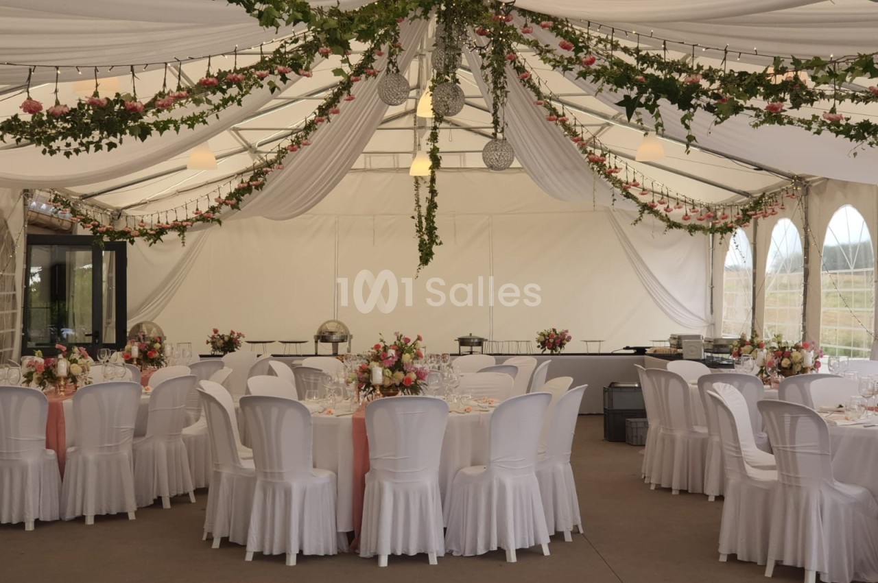 Salle de réception décorée avec des guirlandes de fleurs, des tables rondes dressées et des chaises blanches.